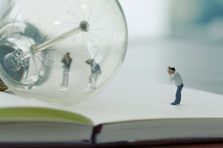 Creative idea concept - miniature photographer with vintage light bulb on open paper notebookの写真素材