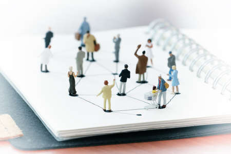 close up of miniature people with social network diagram on open notebook on wooden desk as social media conceptの写真素材