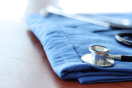 Stethoscope with blue doctor coat on wooden table with shallow DOF evenly matched and backgroundの写真素材
