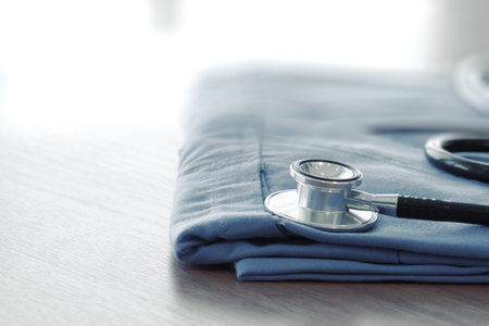 Stethoscope with blue doctor coat on wooden table with shallow DOF evenly matched and backgroundの写真素材