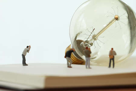 Creative idea concept - miniature photographer with vintage light bulb on open paper notebookの写真素材