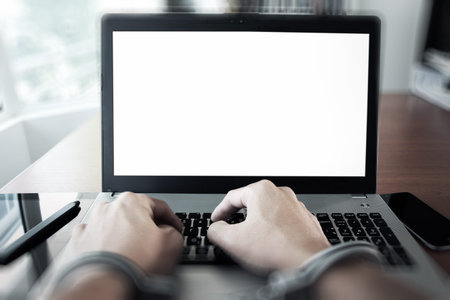 Businessman hand in handcuffs at wooden desk with laptop computer and digital tablet and stylus pen...