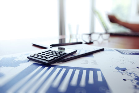 business documents on office table with calculator and digital tablet and man working in the...