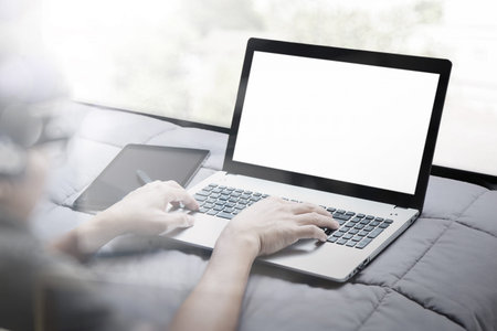 double exposure of young designer working with smart phone and blank screen laptop computer in bed...