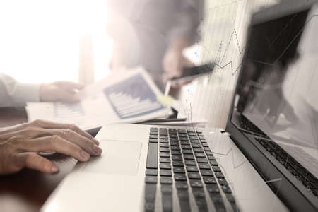 business documents on office table with smart phone and digital tablet and laptop computer and two colleagues discussing data in the backgroundの写真素材