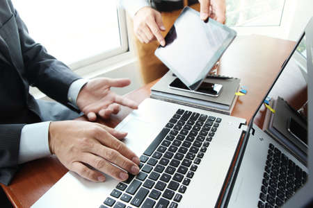 business documents on office table with smart phone and digital tablet and stylus and two colleagues discussing data in the backgroundの写真素材