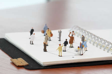 close up of miniature people with social network diagram on open notebook on wooden desk as social media conceptの写真素材