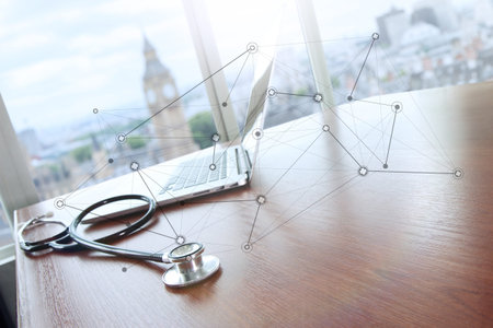 stethoscope and laptop computer on wood table and london bigben blurred background and medical network diagramの写真素材