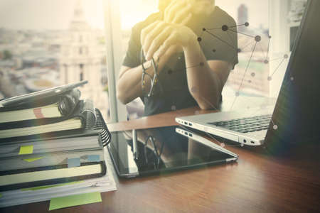Businessman hand holding eyeglasses and laptop computer with overcast effect on wooden desk as concept with social media diagramの写真素材