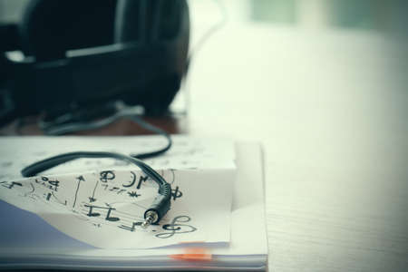Closeup jack of smart phone with headphone on musical notes paper with shallow DOF evenly matched on wooden deskの写真素材