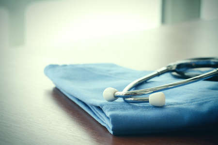 Stethoscope with blue doctor coat on wooden table with shallow DOF evenly matched and backgroundの写真素材