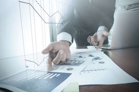 close up of business man hand working on laptop computer with business graph information diagram on wooden desk as conceptの写真素材