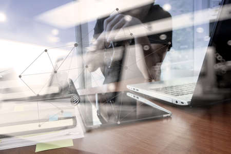 double exposure of designer hand working with digital tablet and laptop and notebook stack and eye glass on wooden desk in office with social network diagramの写真素材
