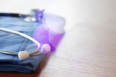Stethoscope with blue doctor coat on wooden table with shallow DOF evenly matched and backgroundの写真素材