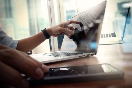 designer hand working and smart phone and laptop on wooden desk in office with london city...