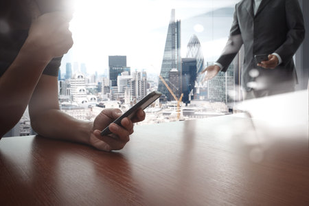 designer hand working and smart phone and laptop on wooden desk in office with london city...