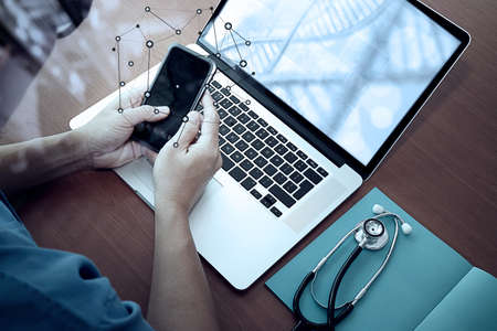 top view of Medicine doctor hand working with modern computer and smart phone with social media network on wooden desk as medical conceptの写真素材