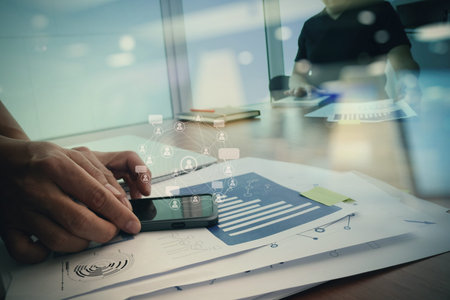 designer hand working and smart phone and laptop on wooden desk in office with social network...