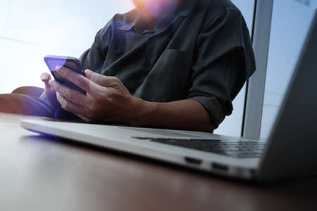 designer hand working and smart phone and laptop on wooden desk in office with london city backgroundの写真素材