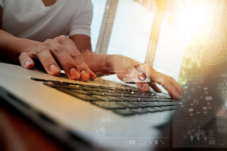 business man hand working on laptop computer on wooden desk with digital business layer effect diagram as conceptの写真素材