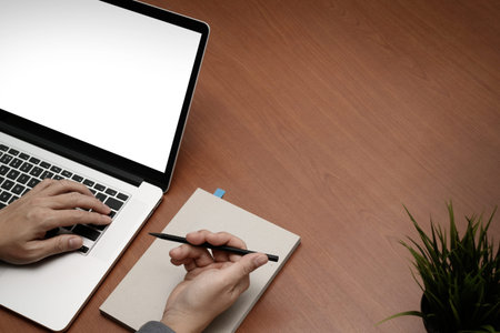 top view of  businessman hand working with new modern blank screen computer on blank book on wooden desk as conceptの写真素材