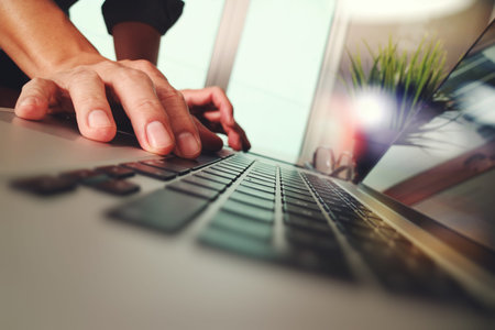 Close up of business man hand working on laptop computer with green plant on wooden desk as concept