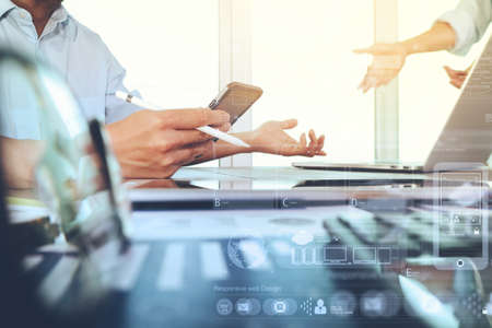 business documents on office table with smart phone and laptop computer and graph business with social network diagram and two colleagues discussing data in the background