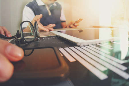 business documents on office table with smart phone and laptop computer and graph business with social network diagram and two colleagues discussing data in the backgroundの写真素材