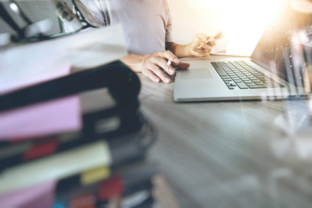 designer hand working with digital tablet and laptop and notebook stack and eye glass on wooden desk...