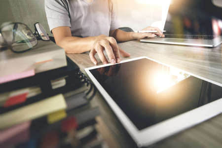 designer hand working with digital tablet and laptop and notebook stack and eye glass on wooden desk in officeの写真素材