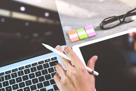 businessman hand working stylus pen and digital tablet computer and memo note and laptop computer. On wooden desk, Photo close up exposure effectの写真素材