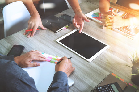 business documents on office table with smart phone and laptop computer and graph business with social network diagram and three colleagues discussing data in the backgroundの写真素材