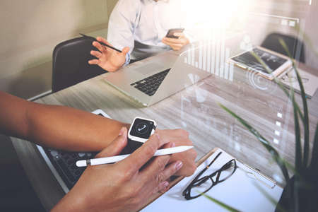 business presentation meeting on office table with smart watch and laptop computer and graph business diagram and three colleagues discussing data in the backgroundの写真素材