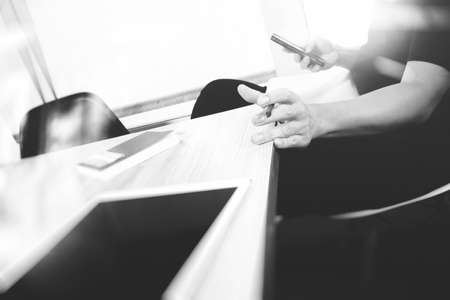 designer hand working and smart phone and blank screen laptop and digital tablet on wooden desk in office, black whiteの写真素材