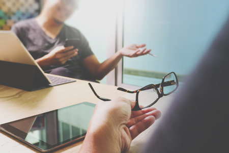 two colleague web designer discussing data and digital tablet and computer laptop with smart phone and design diagram on marble desk as concept,eyeglass holdingの写真素材