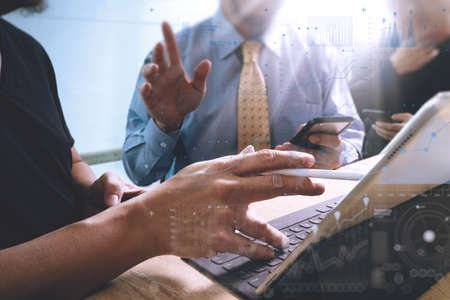 business documents on office table with smart phone and laptop computer and graph financial with social network diagram and three colleagues discussing data in the background,light beamの写真素材