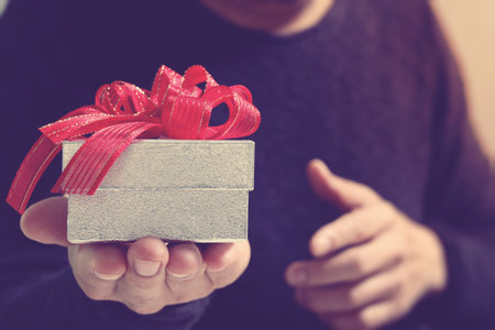 gift giving,man hand holding a gift box in a gesture of giving.blurred background,vintage effectの写真素材