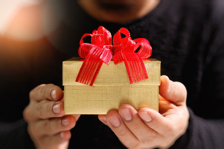 gift giving,man hand holding a gift box in a gesture of giving.blurred background,bokeh effectの写真素材