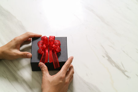gift giving,man hand holding a gift box in a gesture of giving on white gray marble table backgroundの写真素材