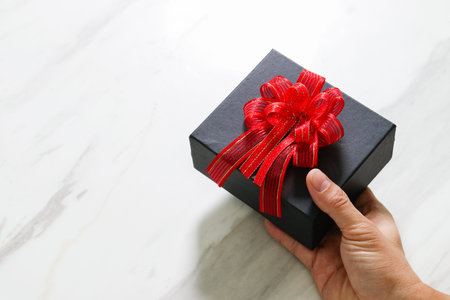 gift giving,man hand holding a gift box in a gesture of giving on white gray marble table background