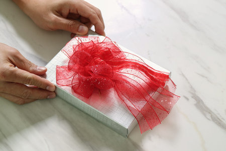 gift giving,man hand holding a silver gift box in a gesture of giving on white gray marble table...