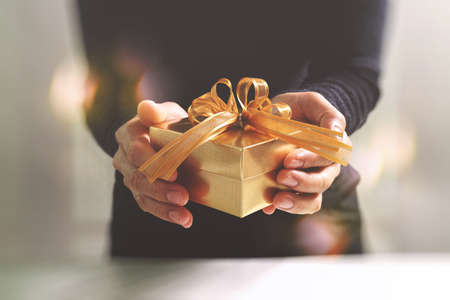 gift giving,man hand holding a gold gift box in a gesture of giving.blurred background,bokeh effectの写真素材