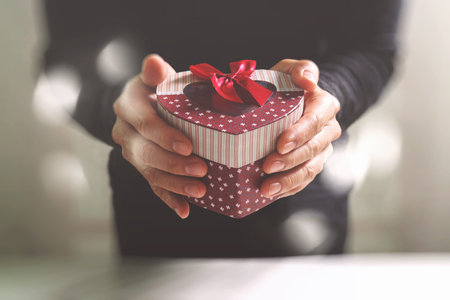 gift giving,man hand holding a heart shape gift box in a gesture of giving.blurred background,bokeh effectの写真素材