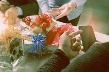 Gift giving Creative Hand using smart phone and co worker choosing gift. Gift delivery,office party,on marble meeting table,vintage effectの写真素材