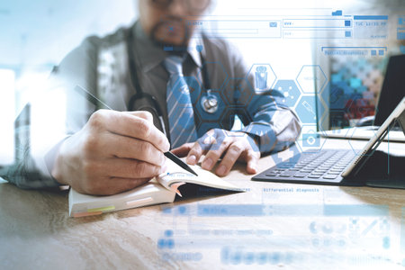 medical doctor writing on notebook and digital tablet docking keyboard with laptop on marble desk,sun flare effectの写真素材