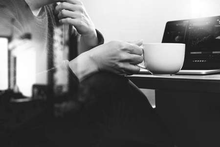 success businessman hand using smart phone,digital tablet docking smart keyboard,coffee cup on wooden desk,black whiteの写真素材
