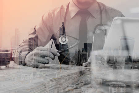Double exposure of smart medical doctor hand working with smart phone,digital tablet computer,stethoscope eyeglass,London architecture bulidingsの写真素材