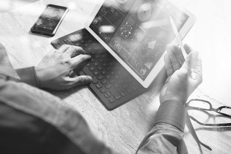 Businessman hand working concept. Photo investor working with new startup project. Digital tablet keyboard dock screen computer design smart phone using. Eyeglass on marble desk. Sun flare effect. black whiteの写真素材