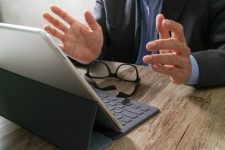 success businessman hand using eyeglass,digital tablet docking smart keyboard on wood desk