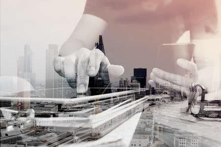Double exposure of Designer hand using mobile payments online shopping,omni channel,in modern office wooden desk,London city buildings,eyeglassの写真素材